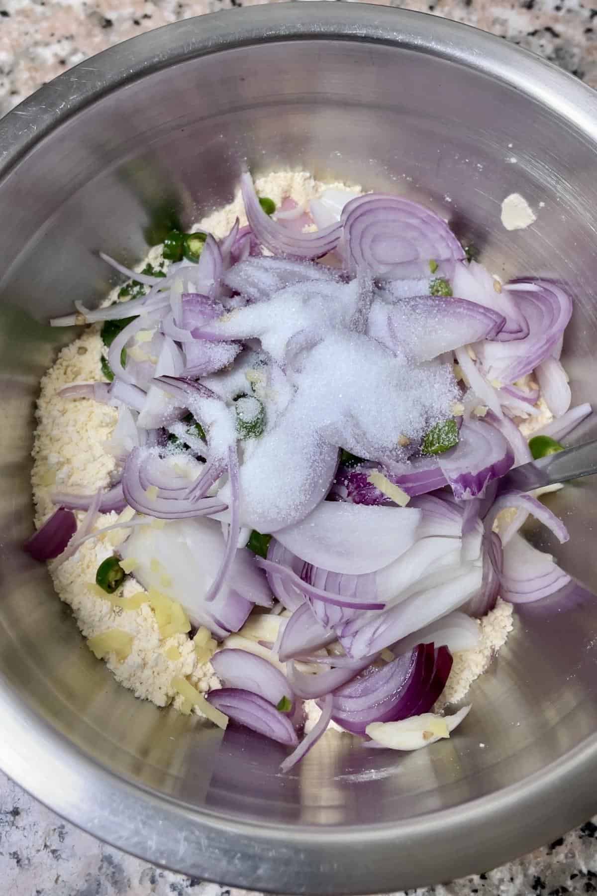A bowl with flour mixture and chopped onions and other aromatics. 