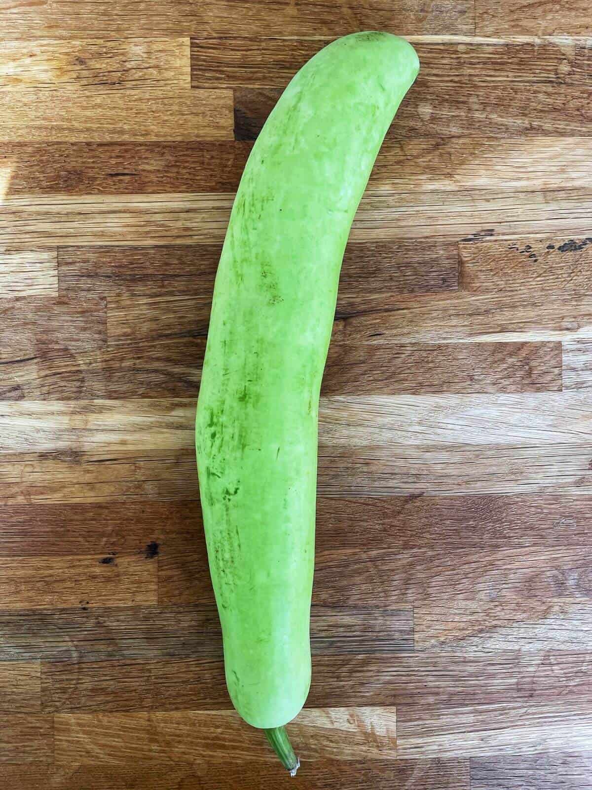 A whole bottle gourd on a cutting board. 