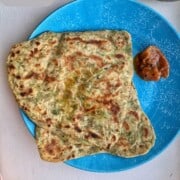Two lauki paratha on a blue plate with some pickle by side.