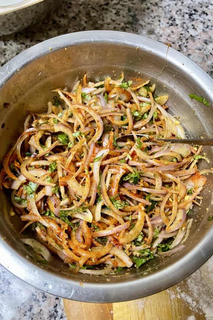 A bowl of  thinly sliced onions coated with spices and gram flour. 