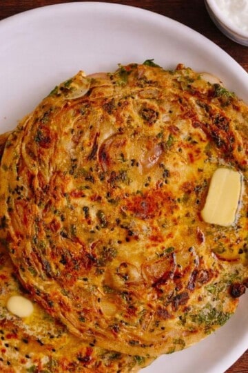 Two onion parathas topped wtih a knob of butter served on a white round plate.