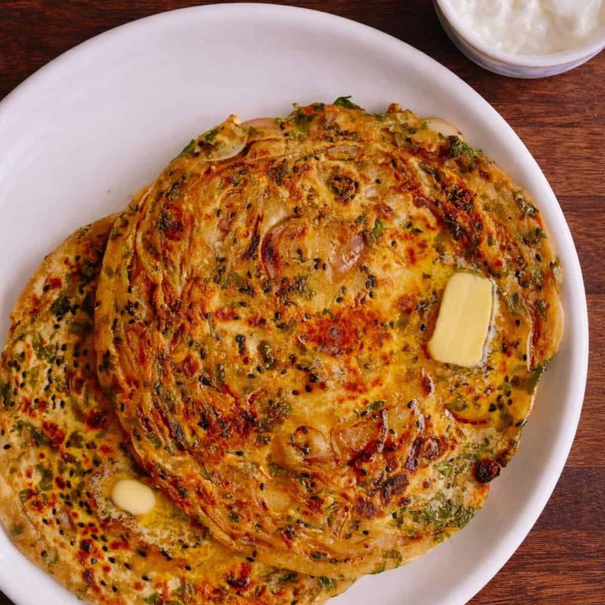 Two onion parathas topped wtih a knob of butter served on a white round plate.