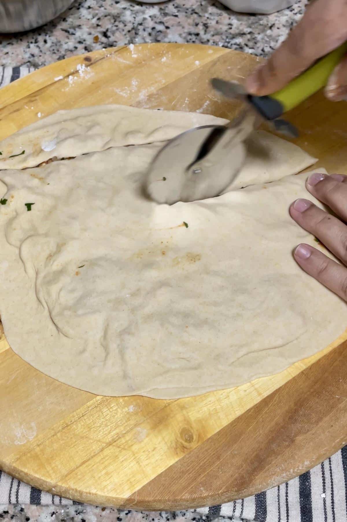 Slicing the stuffed dough into strips using pizza cutter. 