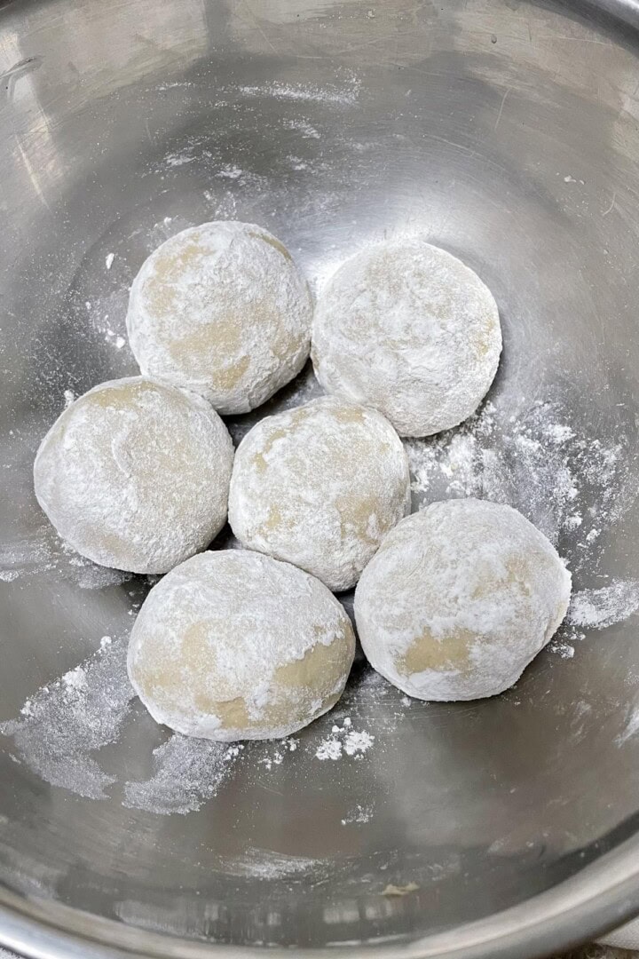 Six dough balls smoothed and dusted resting.