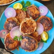 Fried chicken shami kababs with onions and lime on a blue plate.