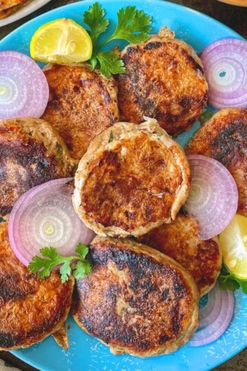 Fried chicken shami kababs with onions and lime on a blue plate.
