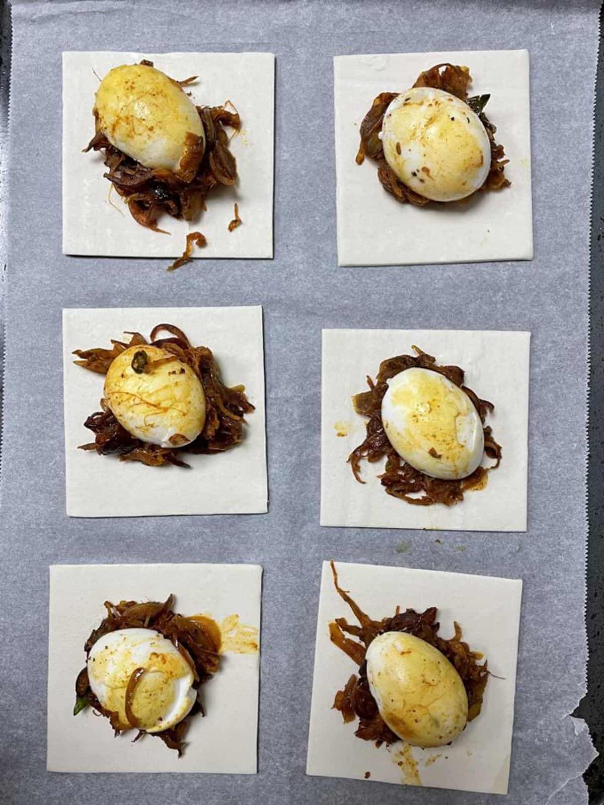 halved boiled eggs placed on spiced onion masala on puff pastry squares ready to fold and seal