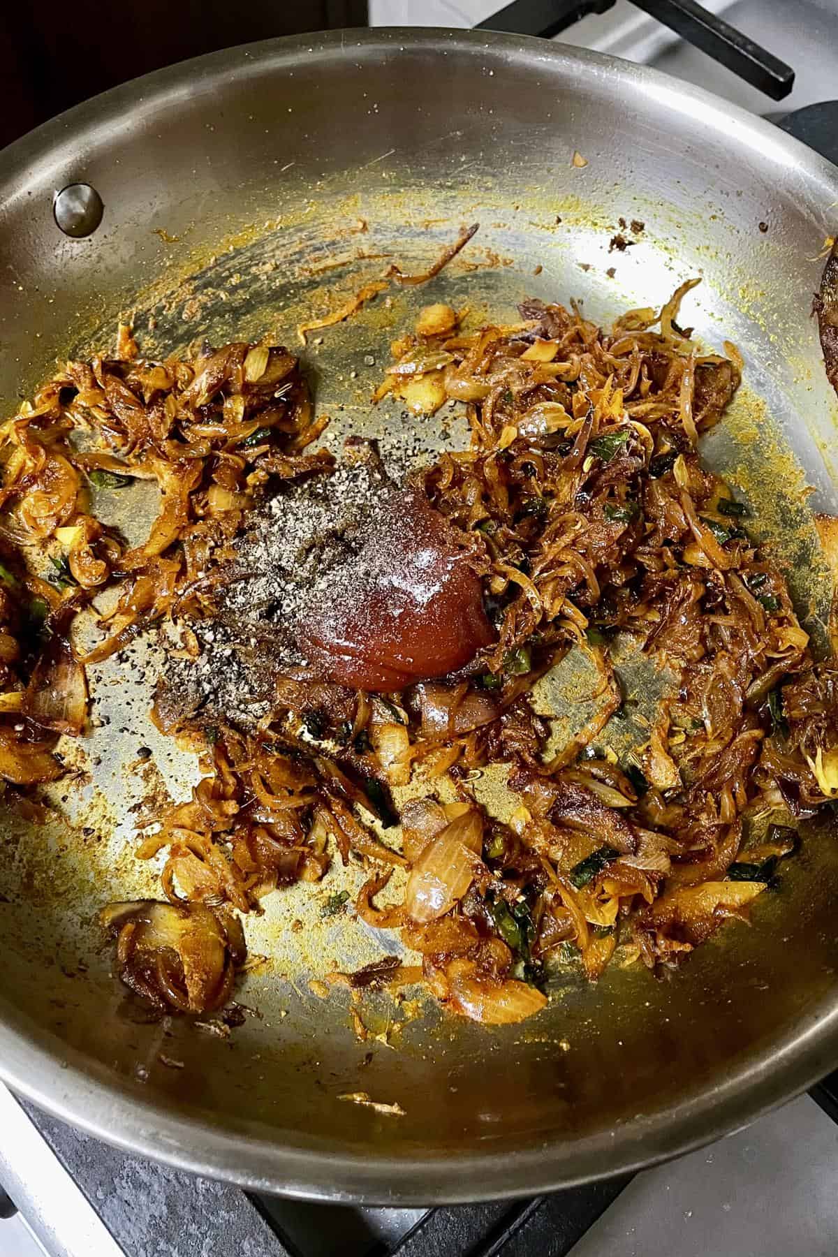 deeply caramelised onion masala with ketchup and ground pepper being added to pan
