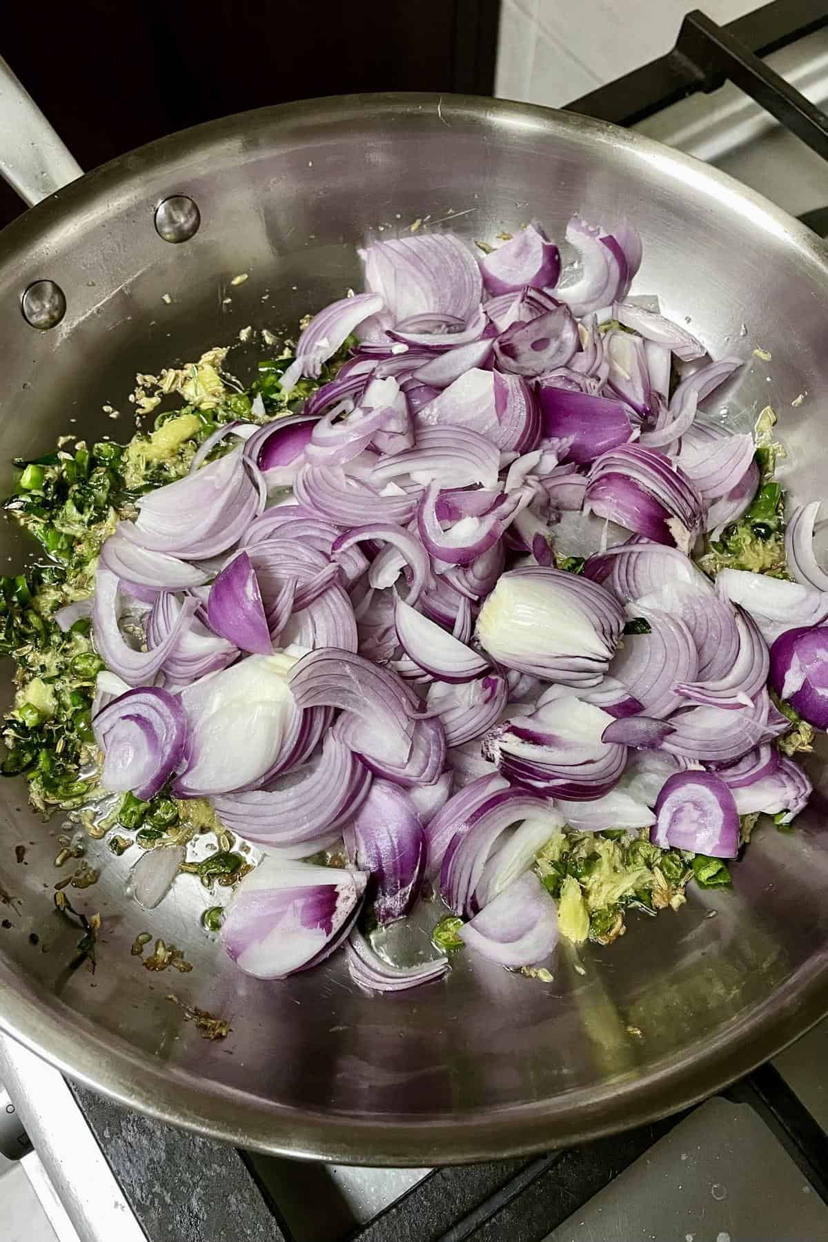 sliced red onions added to pan with green chillies and ginger for Kerala egg puff masala