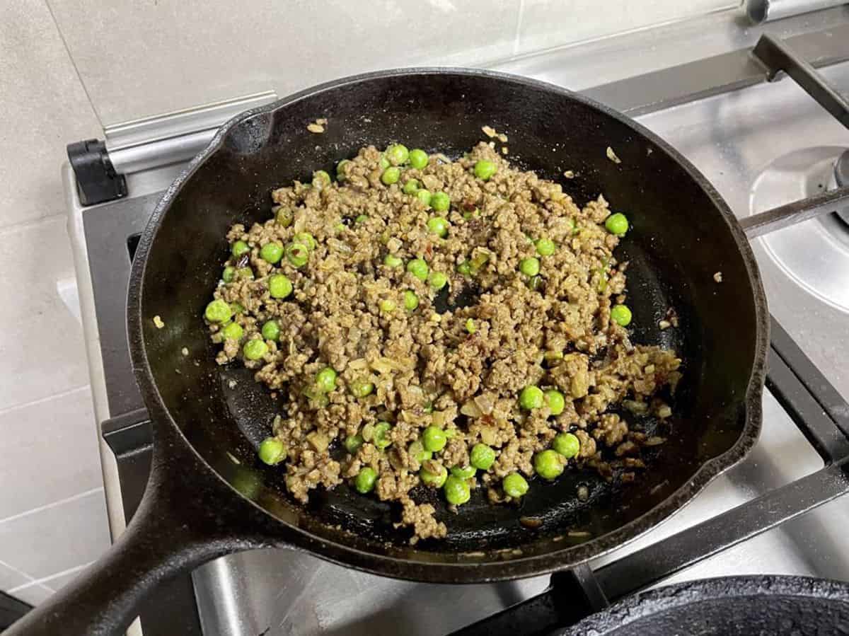 thawed green peas over browned minced meat in skillet