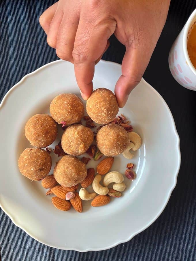 a plate of seven ari unda aka rice balls served with cashewnuts and almonds while a hand is picking one of the rice balls.