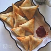 nine baked samosas served in a fluted bowl with a mug of chai and ketchup