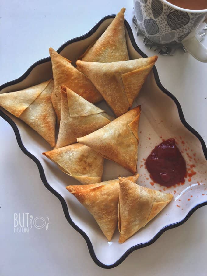 nine baked samosas served in a fluted bowl with a mug of chai and ketchup