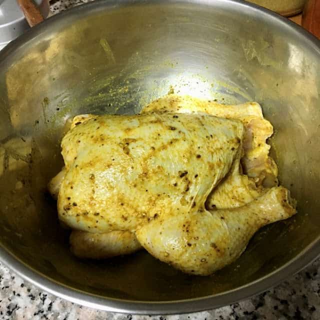 whole chicken with skin marinated with mandi spice sitting in a bowl.