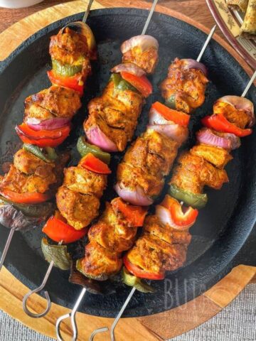 four skewers of chicken tikka with bell peppers on a cast iron pan