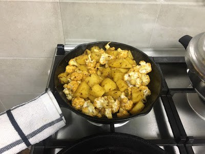 potato chunks, cauliflower florets being cooked in a cast iron skillet. 