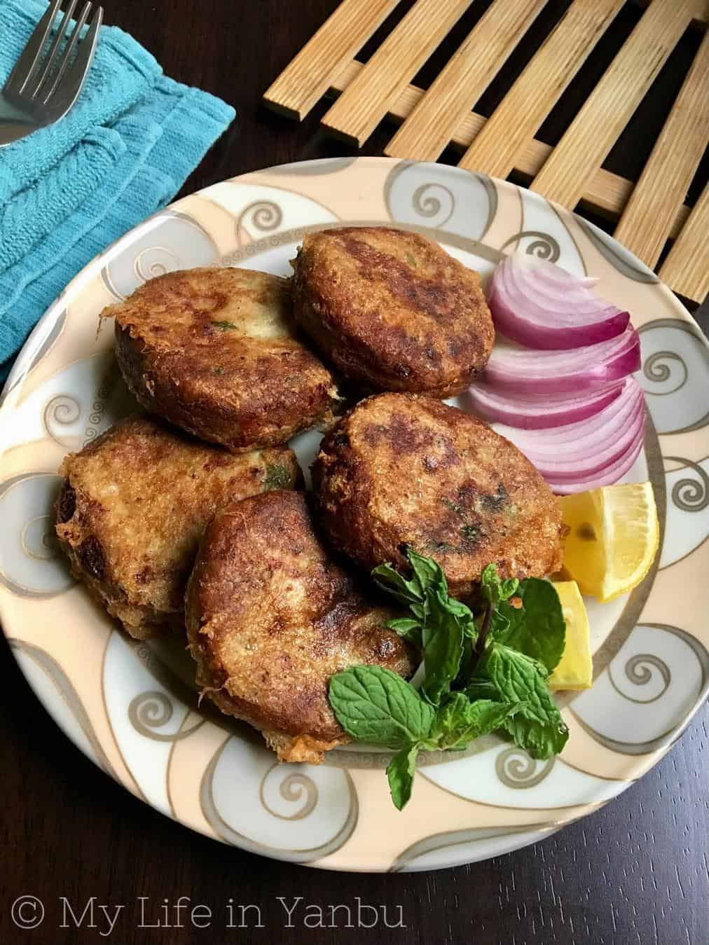 A plate full of shami kebabs with lime wedges and onion chunks