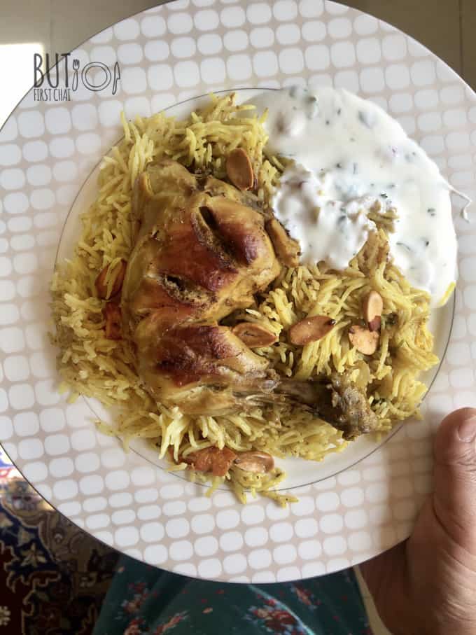 a plate of rice topped with a roasted chicken leg and some yoghurt dip in the side. 