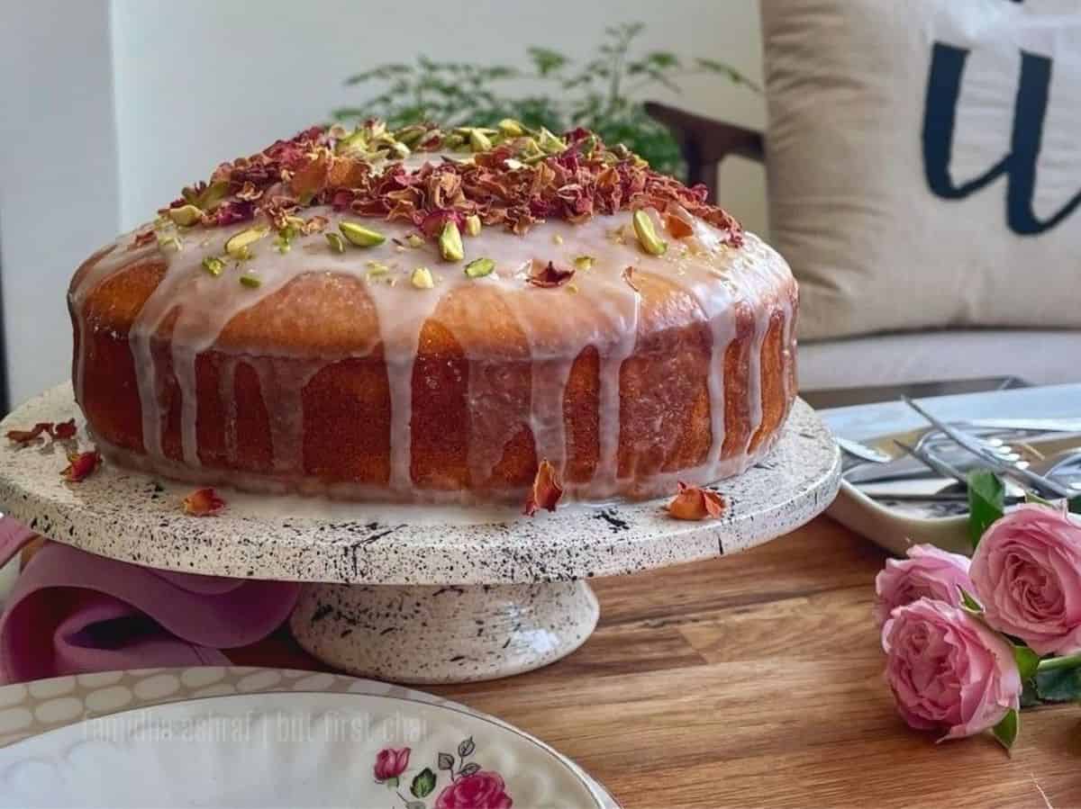 A whole persian love cake on a cake stand with pink roses.