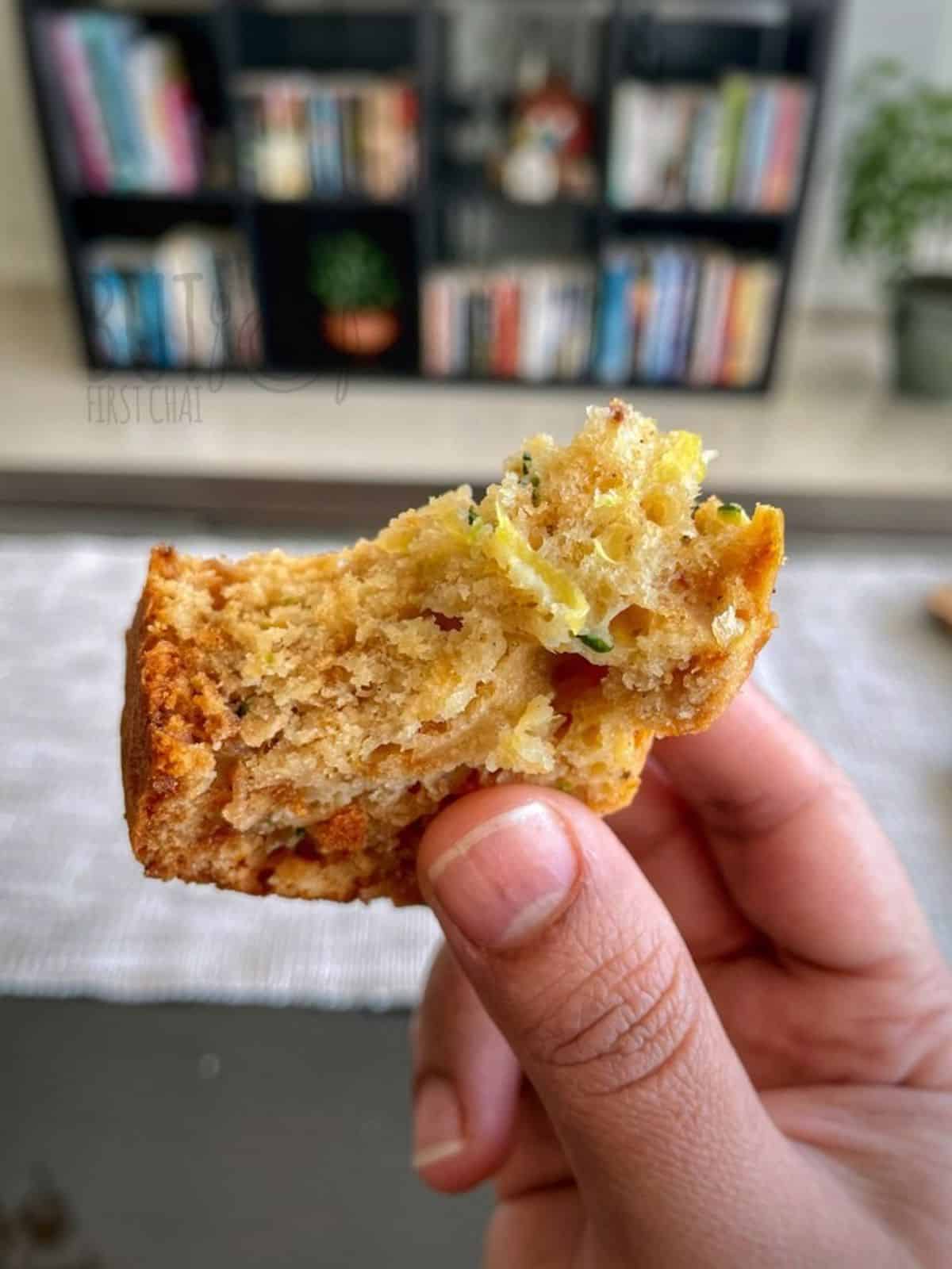 A small piece of half bitten zucchini bread slice in hand.