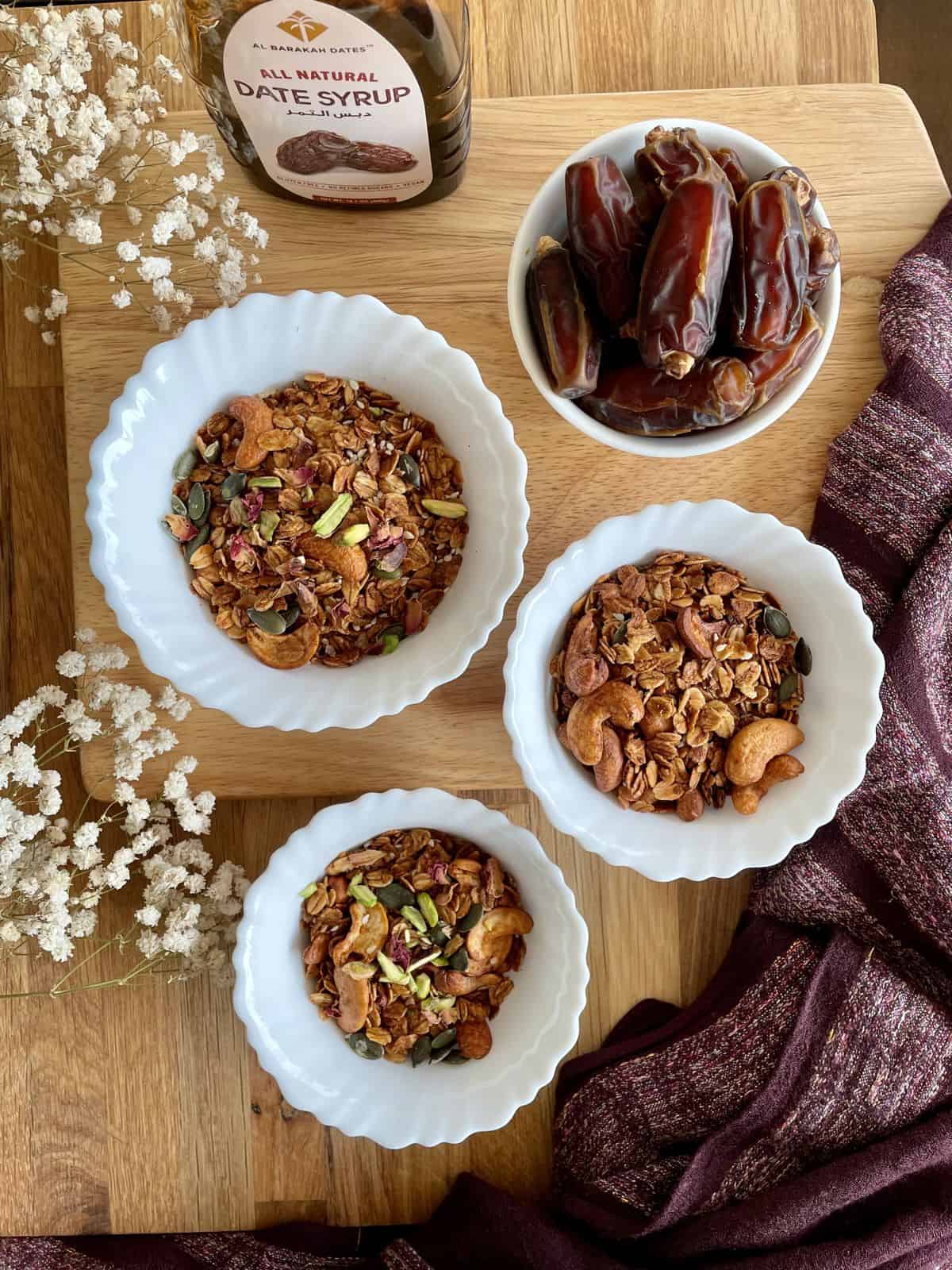 Three small bowls filled with date paste granola along with a bowl of dates with the bottle of date paste.