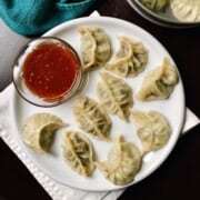 A plate of beef momos with a small bowl of sweet chilli sauce served.