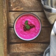 A small bowl of beetroot raita with yogurt garnished with mint leaves.