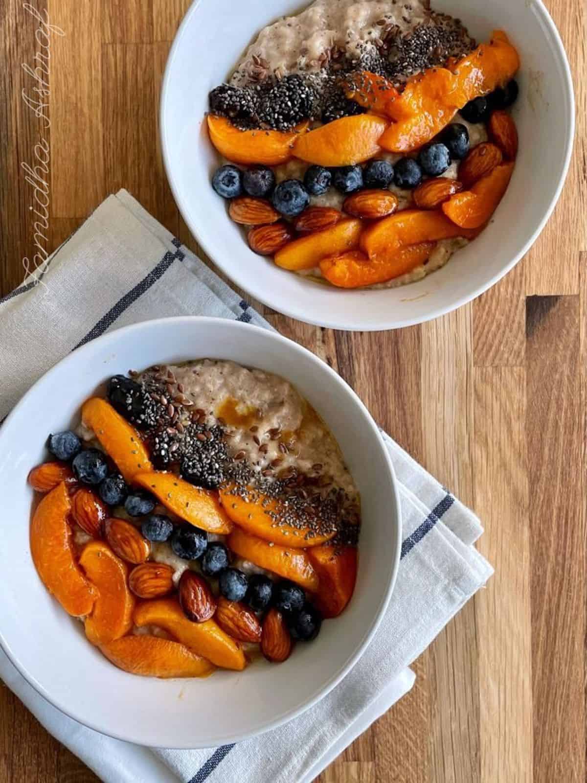 two bowl of oatmeal topped with roasted apricots and nuts