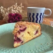 a wedge of cherry tea cake on a plate with a cup of tea