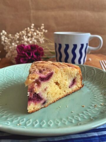 a wedge of cherry tea cake on a plate with a cup of tea