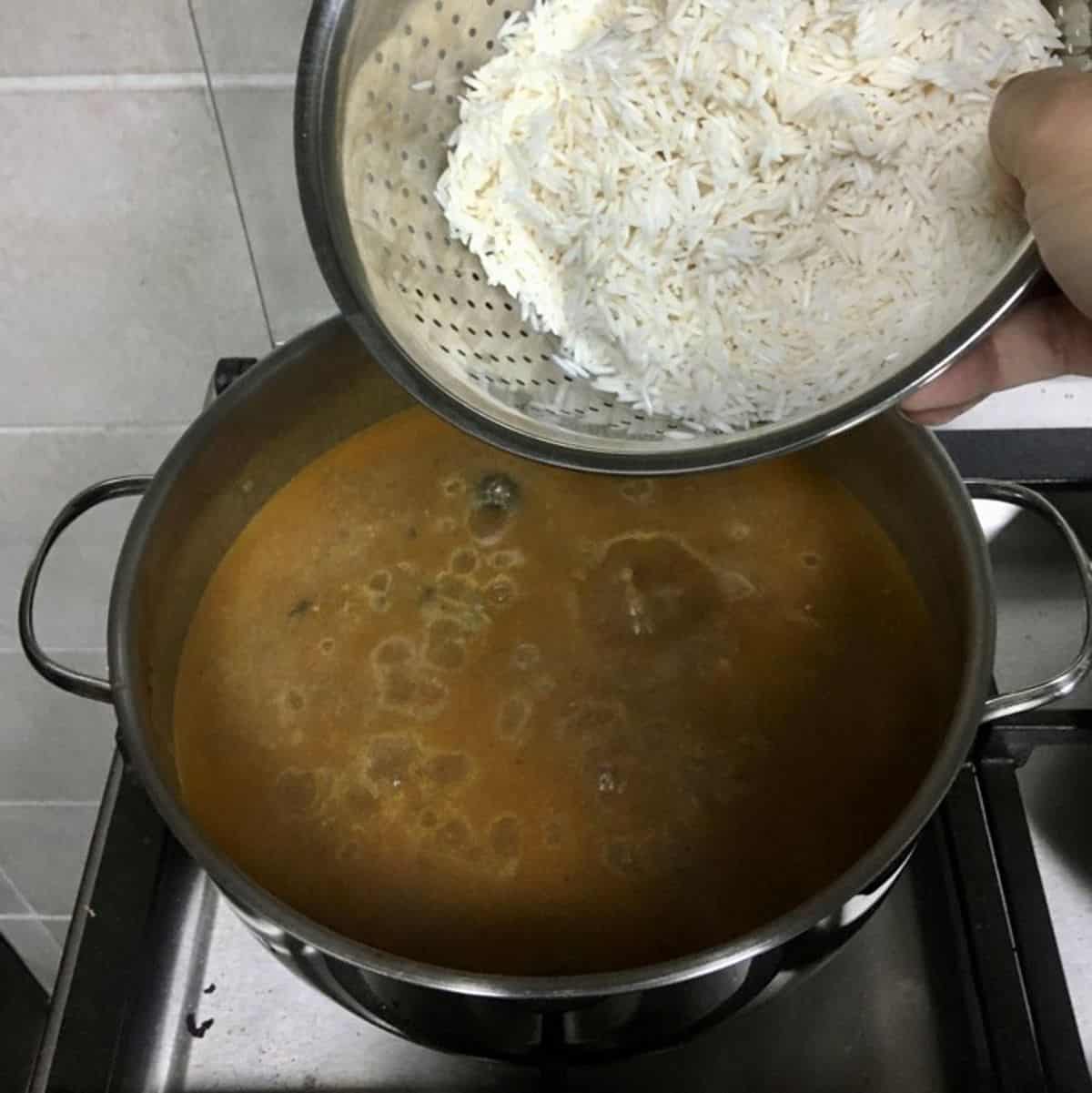 Adding soaked and drained basmati rice to kabsa broth.