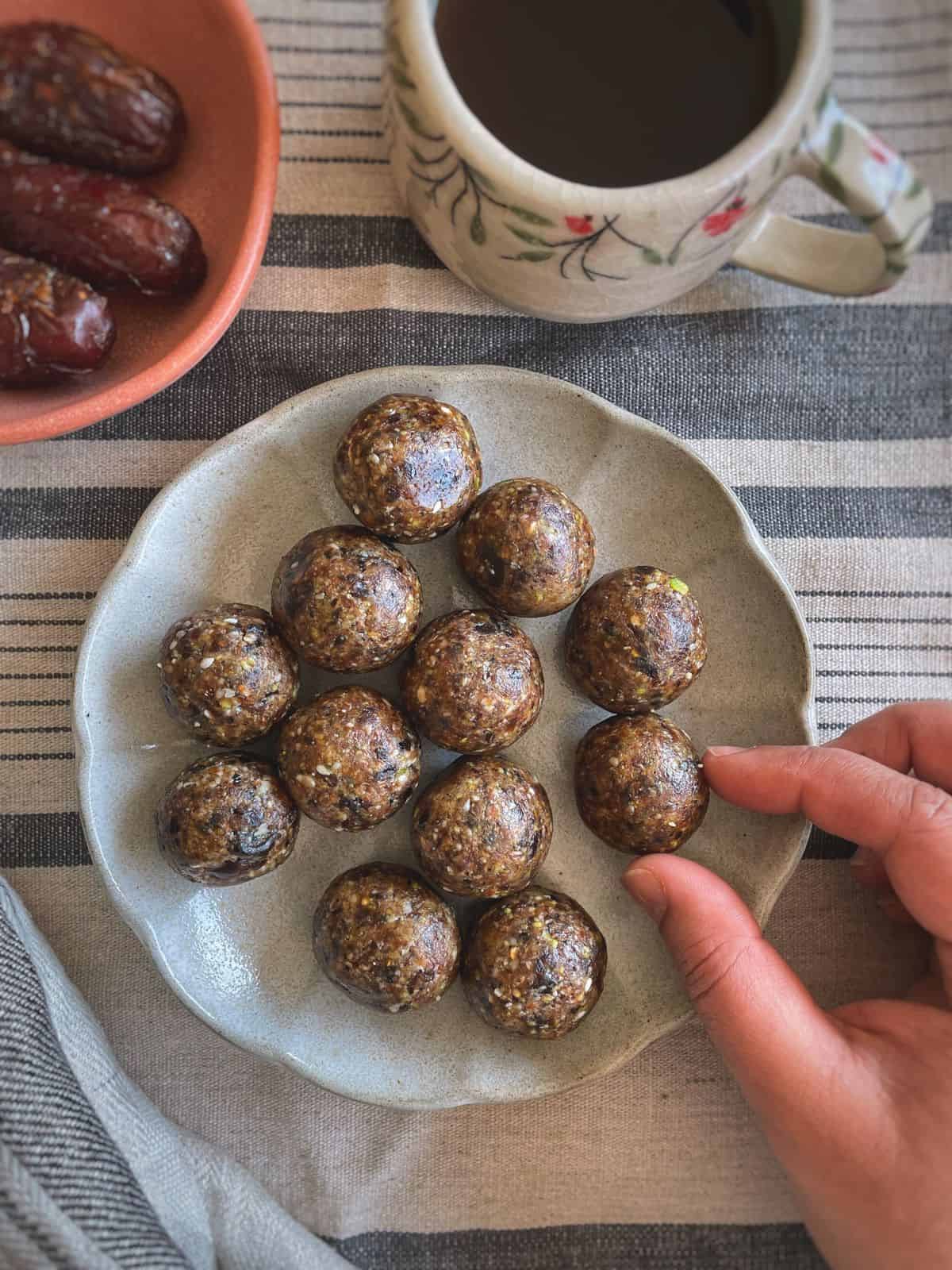 A plate of energy balls with a hand picking one of them.