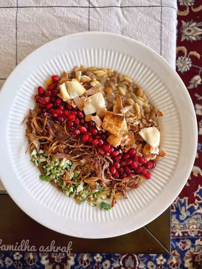 a bowl of horaa osbao garnished with fried onion, fried pita and pomegranate
