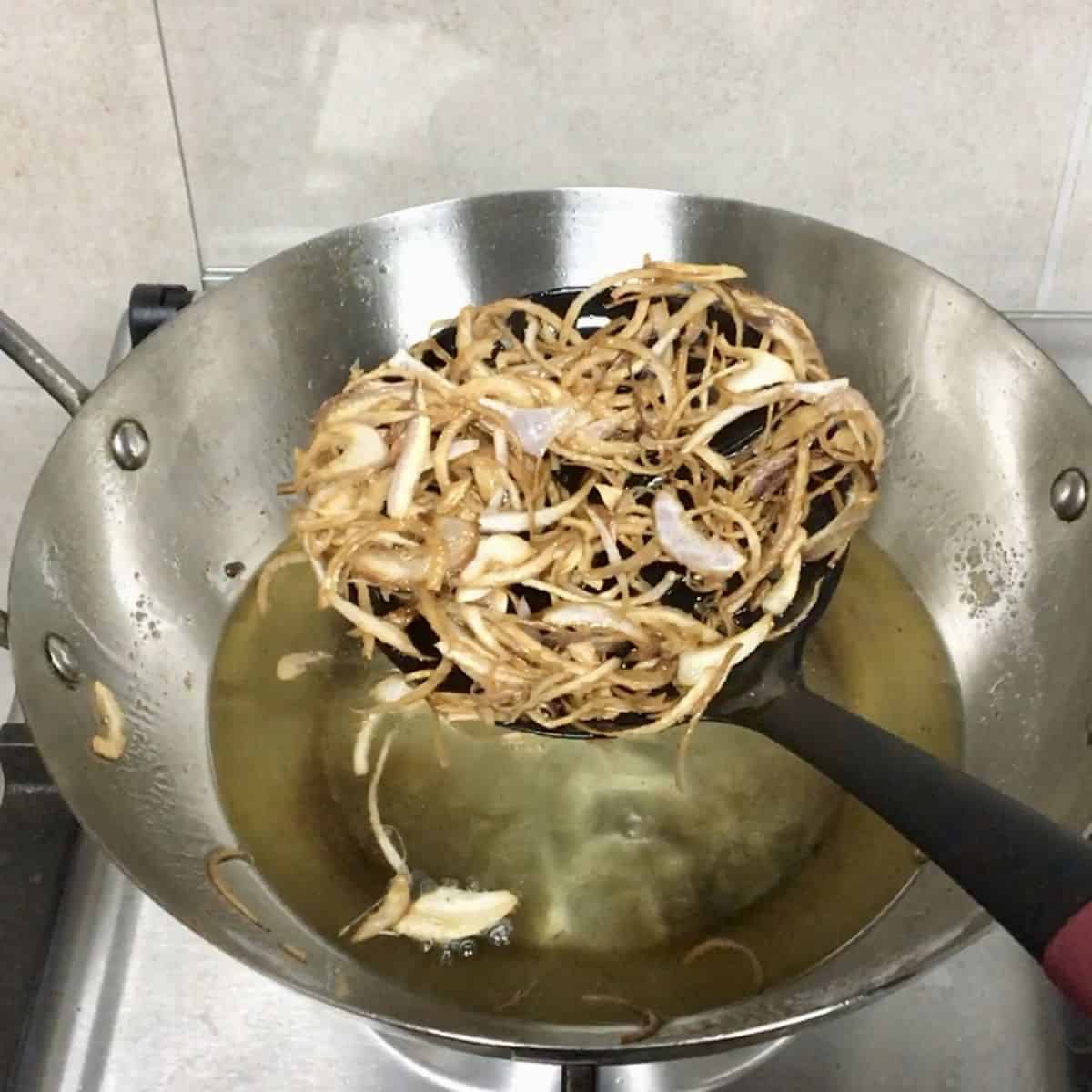 fried onions being scooped out of hot oil