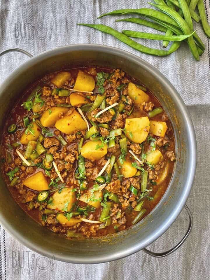 A pot of minced meat potata and cluser beans ready to be served with a stack of kulcha.