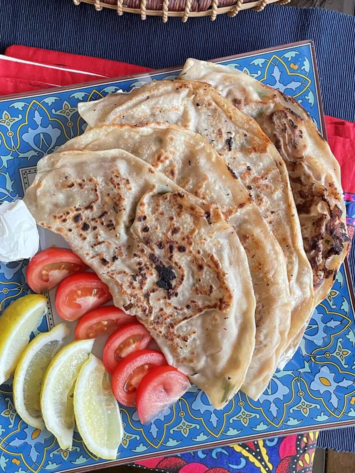 A platter of kiymali Turkish gozleme served with fresh tomatoes and lemon wedges.