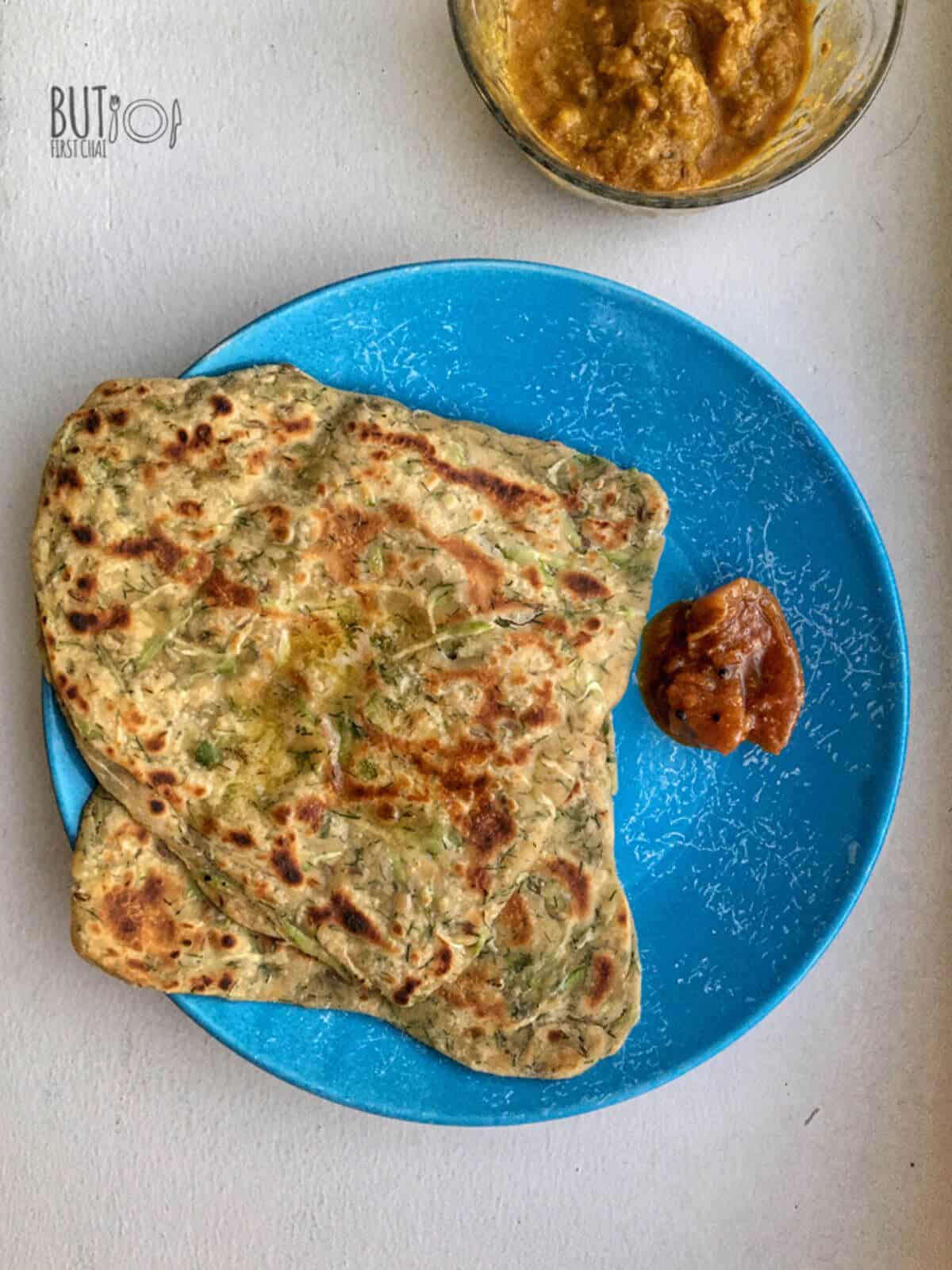 A plate with two lauki paratha with pickle in the side. 
