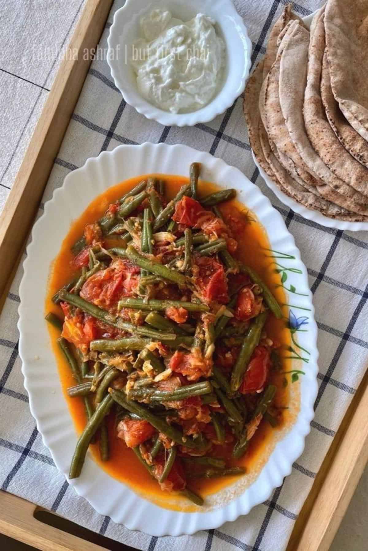 loubieh bi zeit in a platter along side a small bowl of labneh and a stack of pita