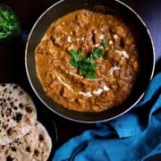 murgh makhani sauce served in a pan with a few butter naan bread.