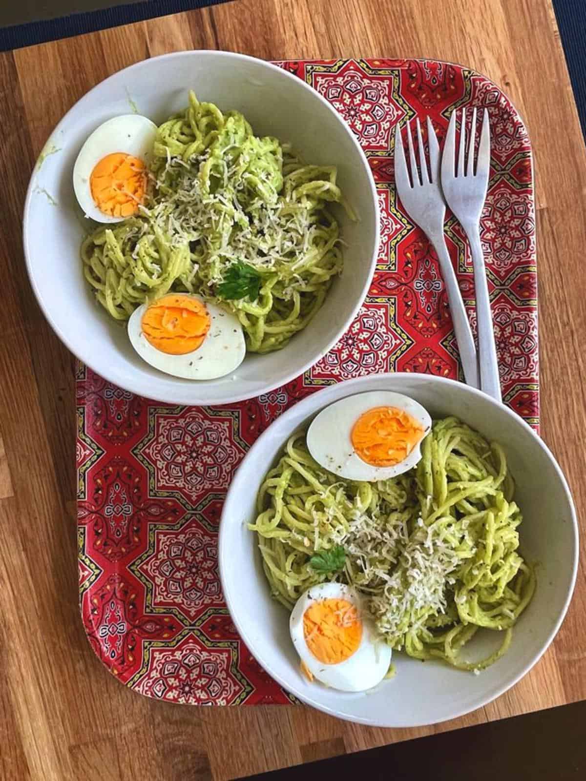 Two bowls of spaghetti with avocado sauce and boiled eggs topped with grated parm.