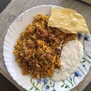 A plate of Tamil style mutton biryani served with raita and pappad.
