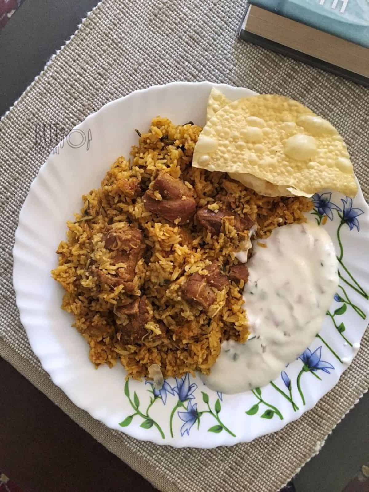 a plate of mutton biryani Tamilnadu style served with raitha, pappadam