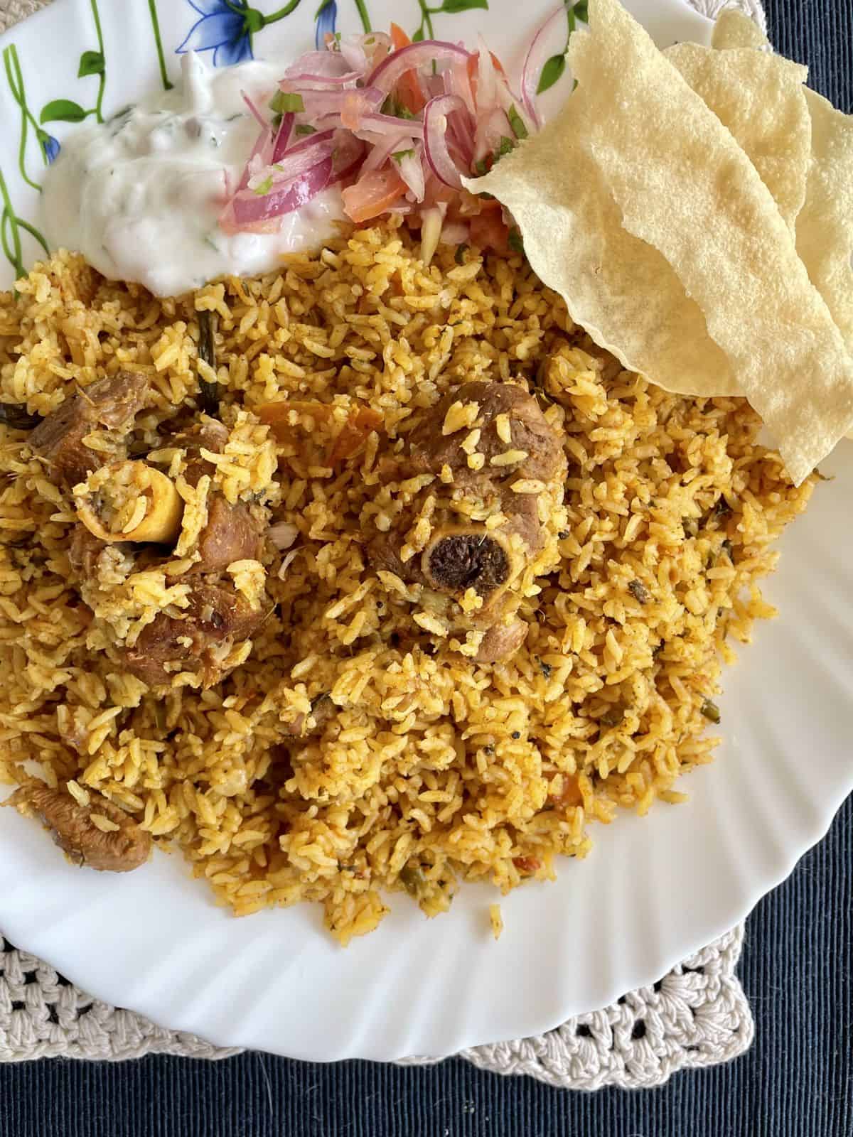 a plate of mutton biryani Tamilnadu style served with raitha, pappadam