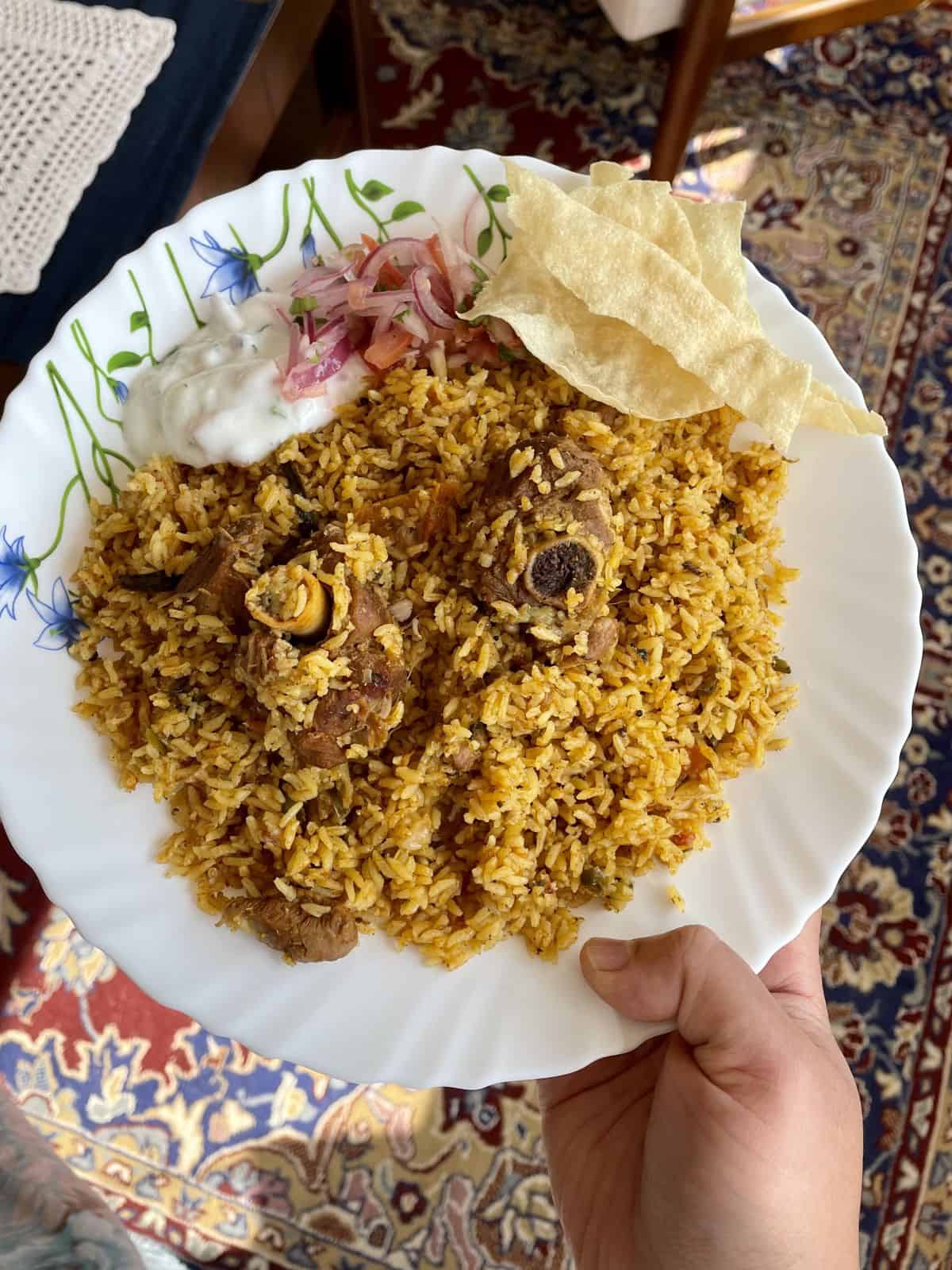 a plate of biryani with pappad and raita