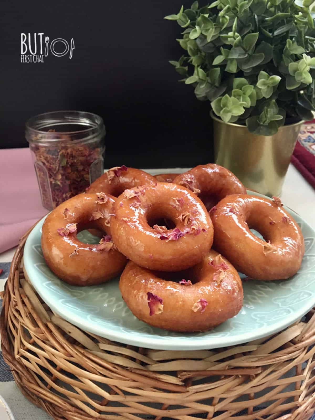 rose glazed yeast donuts stacked on a plate garnished with dried rose petals.