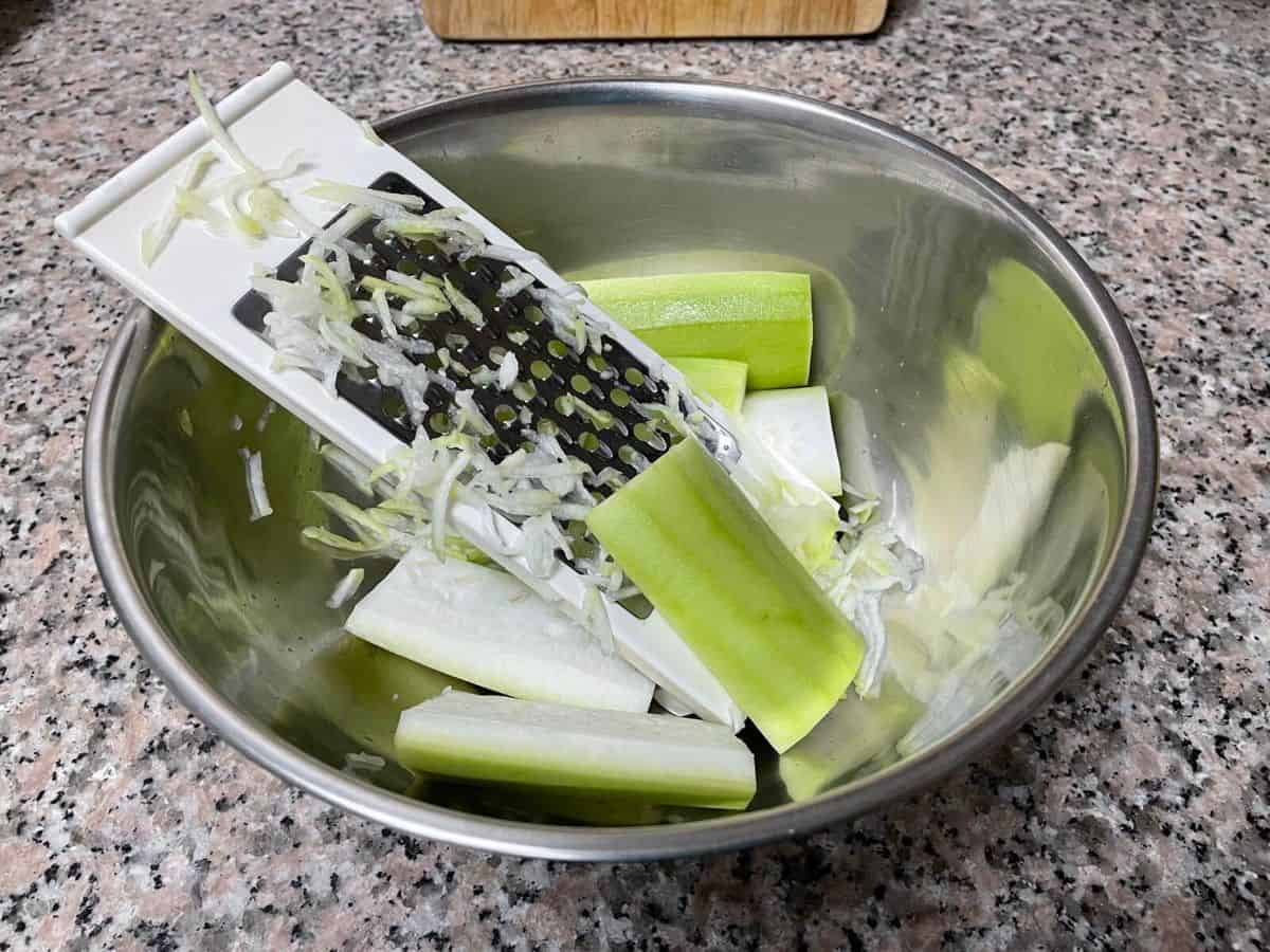A bowl of bottle gourd pieces with a grater.