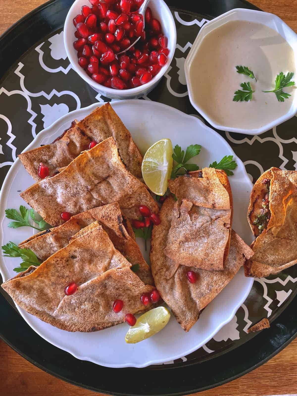 stack of arayes in a plate with tahini sauce and a bowl of pomegranate 
