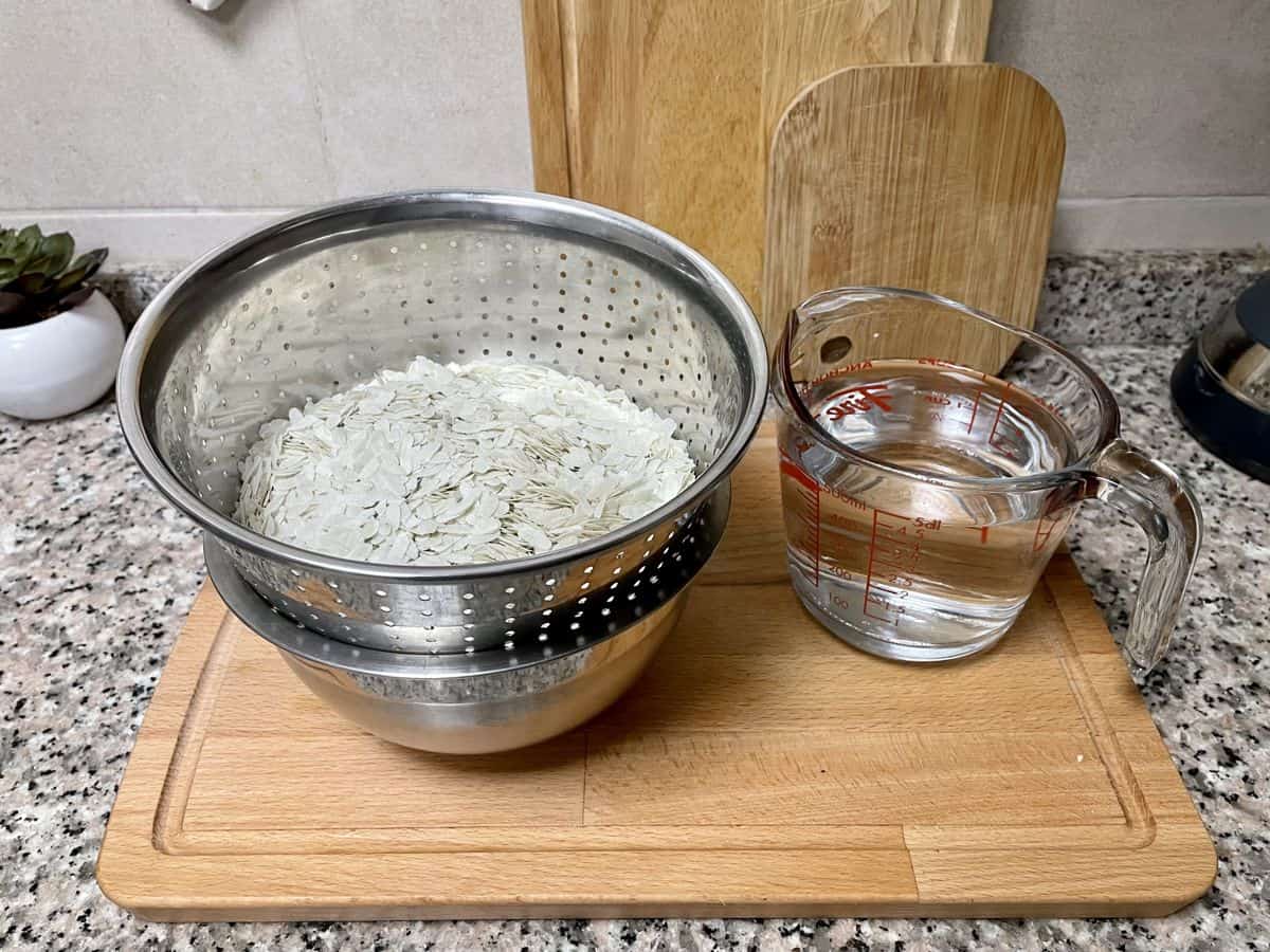 rice flakes in a colander with a jar of water next to it. 