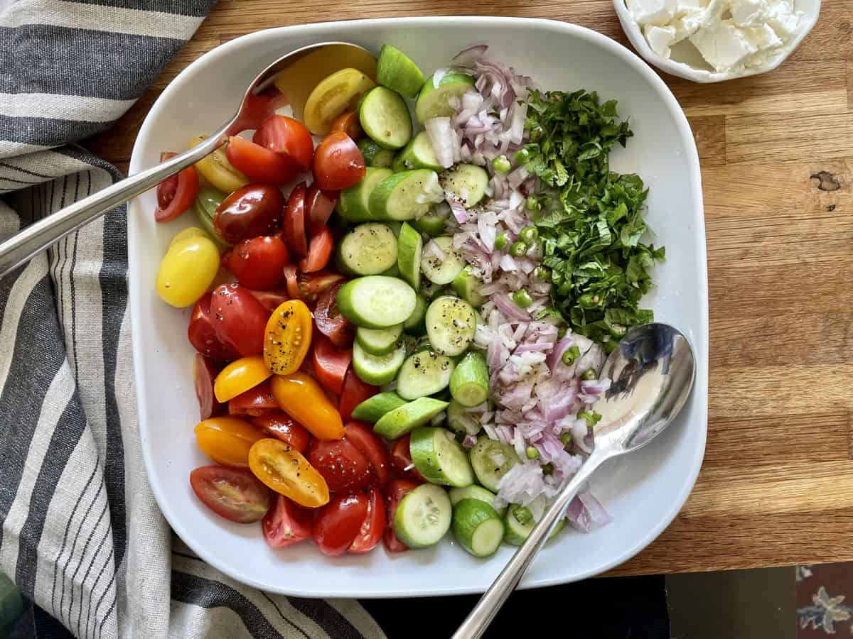 A shallow bowl of Cucumber tomato salad with dressing poured all over. 