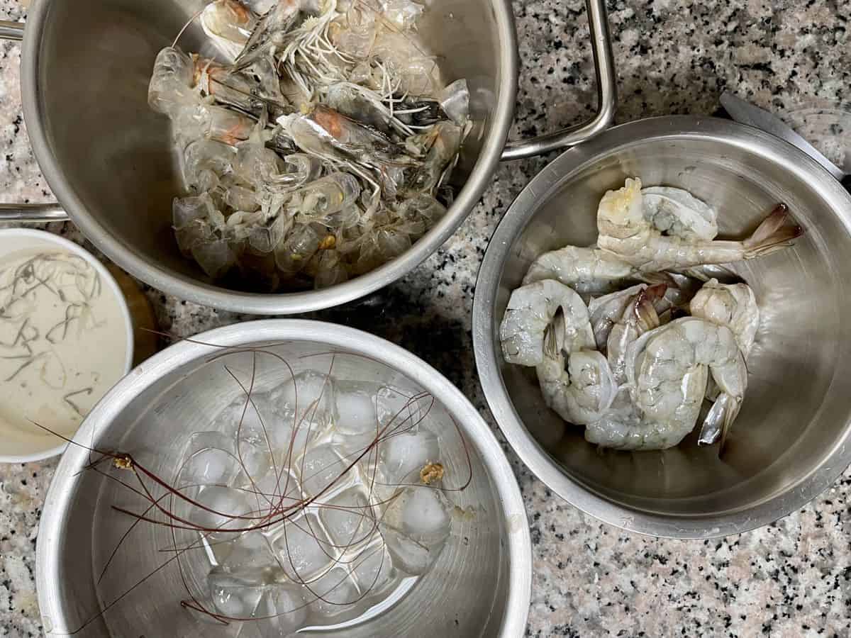 Prawns head and shells in a pot. Peeled and deveined prawns in another bowl. 